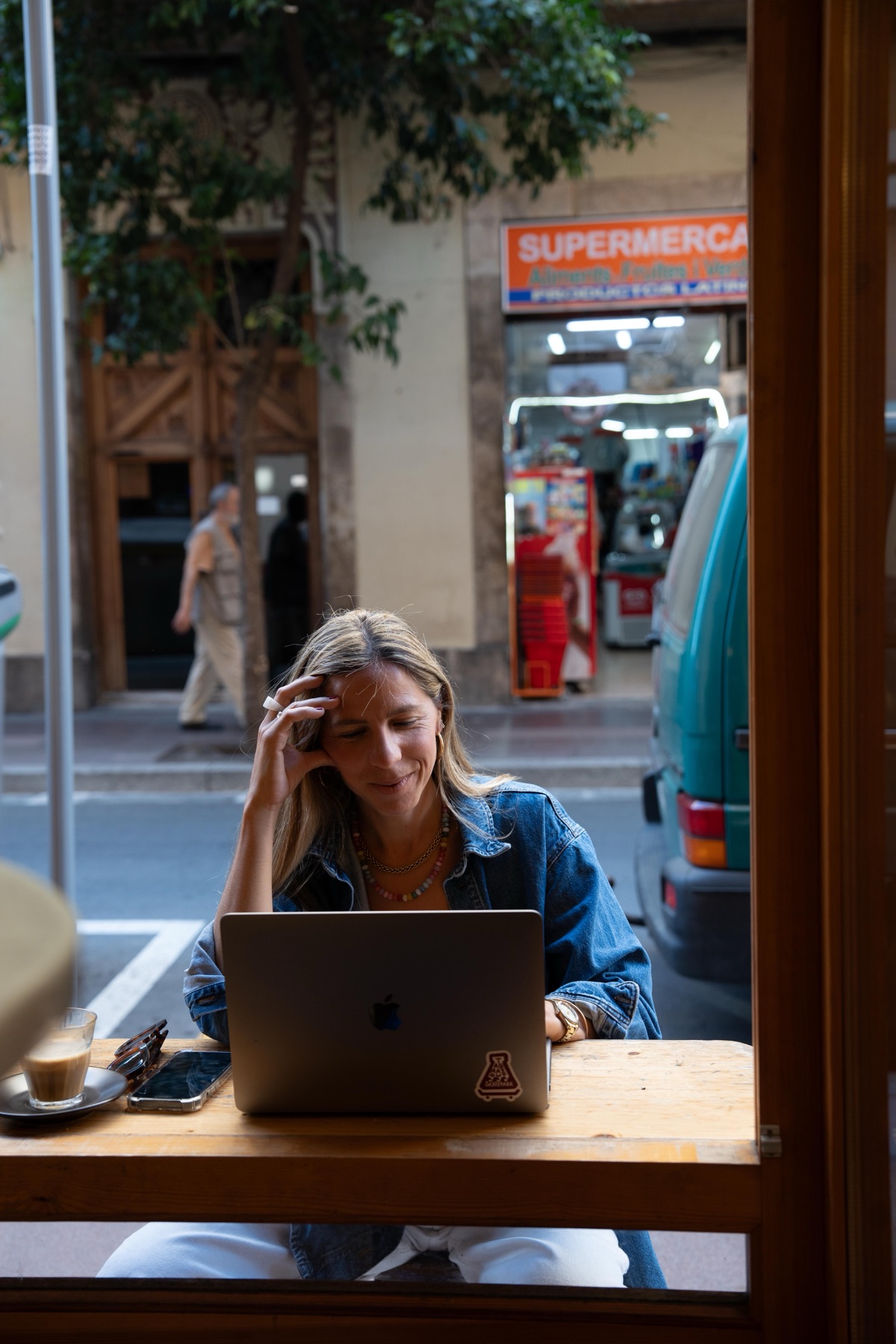 Claudia trabajando con el portátil junto a una ventana, con un café